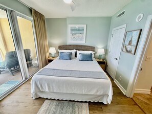 Een slaapkamer met een groot bed, een glazen schuifdeur, een tafeltje met een lamp en een ingelijst schilderij aan de muur.