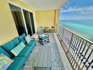 Een balkon met een bank, stoelen en een tafel, met uitzicht op een strand met helder water.