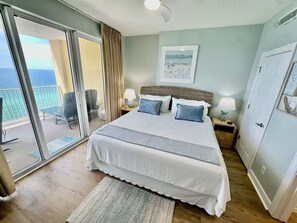 Ein Schlafzimmer mit einem Bett, zwei Nachttischen, einem Fenster mit Blick aufs Meer und einer Tür.