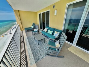 Ein Balkon mit Blick auf den Strand, eine Couch, ein Sessel und ein kleiner Tisch.