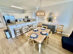 Eine moderne Küche mit weißen Schränken, einem Edelstahlkühlschrank und einem Essbereich mit einem Holztisch, gedeckt für vier Personen.