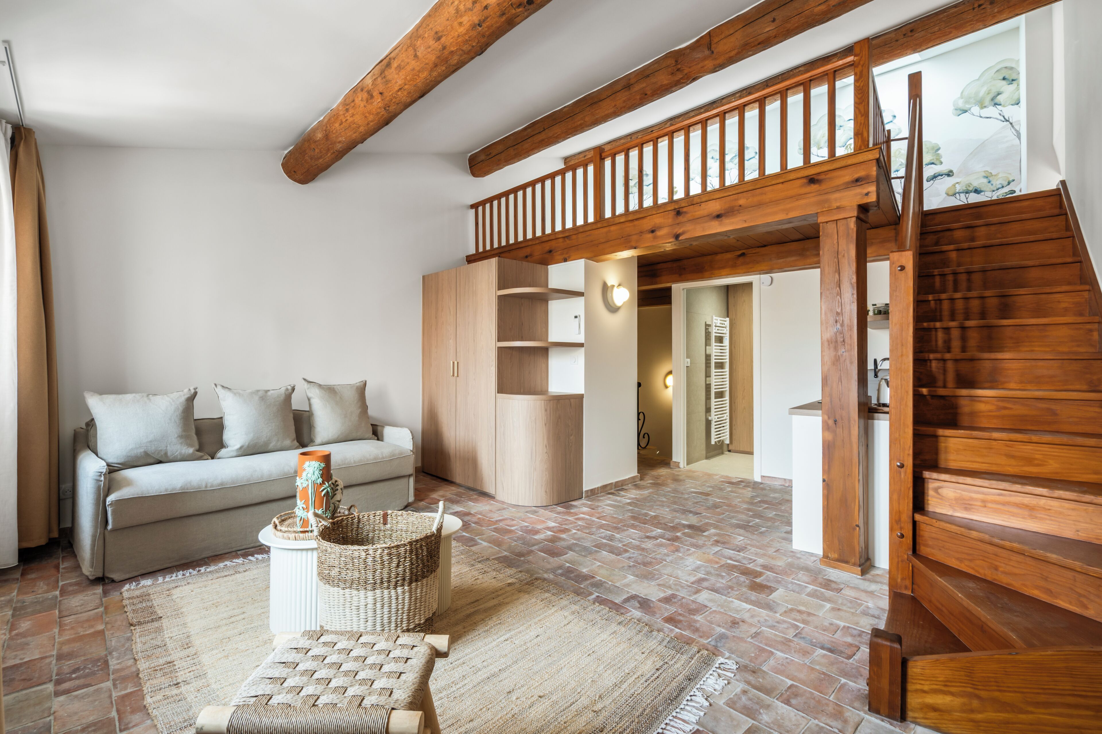 Un amplio salón con una escalera de madera, un sofá, una mesa de centro y una cesta.