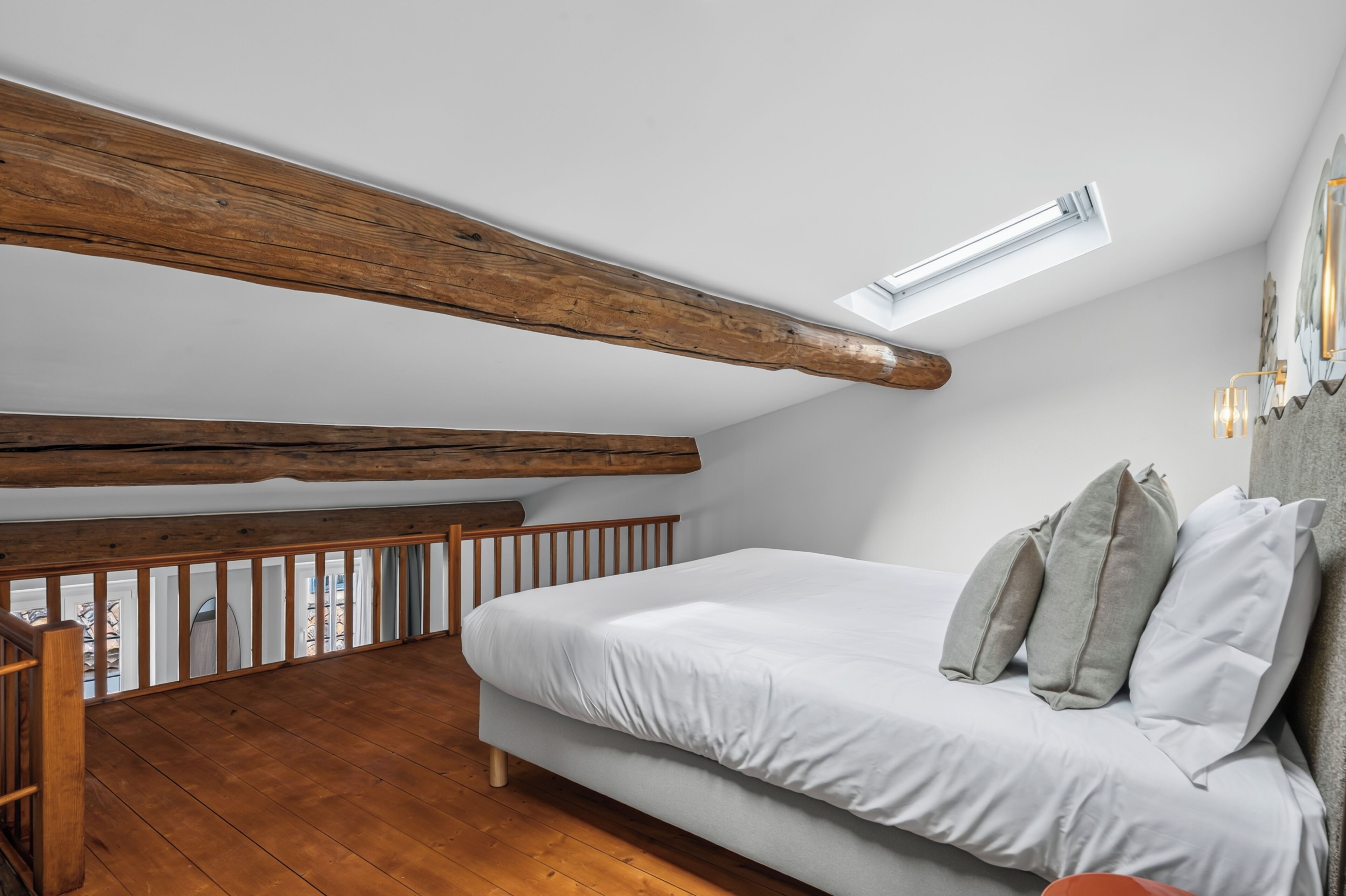Een slaapkamer met een schuine kap, houten balken, een bed met kussens en uitzicht op de omgeving.