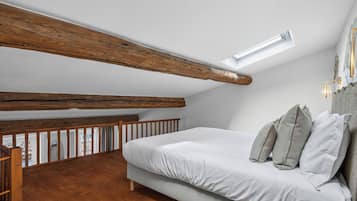 Een slaapkamer met een schuine kap, houten balken, een bed met kussens en uitzicht op de omgeving.