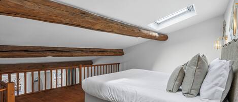Un dormitorio con techo inclinado, vigas de madera, una cama con almohadas y vistas al exterior.