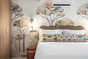 Un dormitorio con cama, almohadas, aire acondicionado de pared y un mural de temática natural.