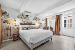 A modern bedroom with a large bed, a small table, a chair, and a wall mural. - Theava Collection -Citadelle- St Tropez (Saint-Tropez)