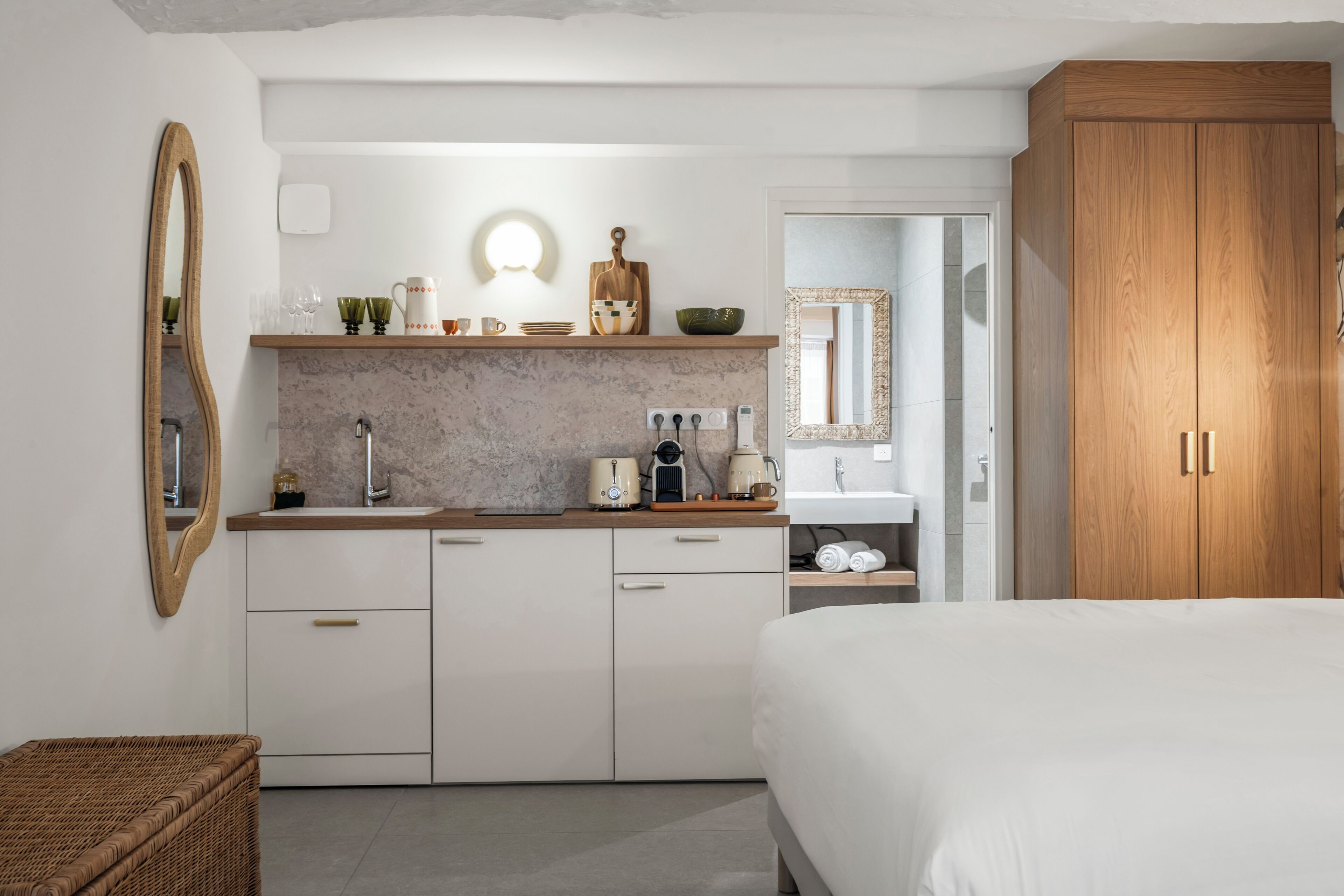 Un dormitorio moderno con una cama grande, un armario de madera, una cocina integrada con encimera y un espejo.