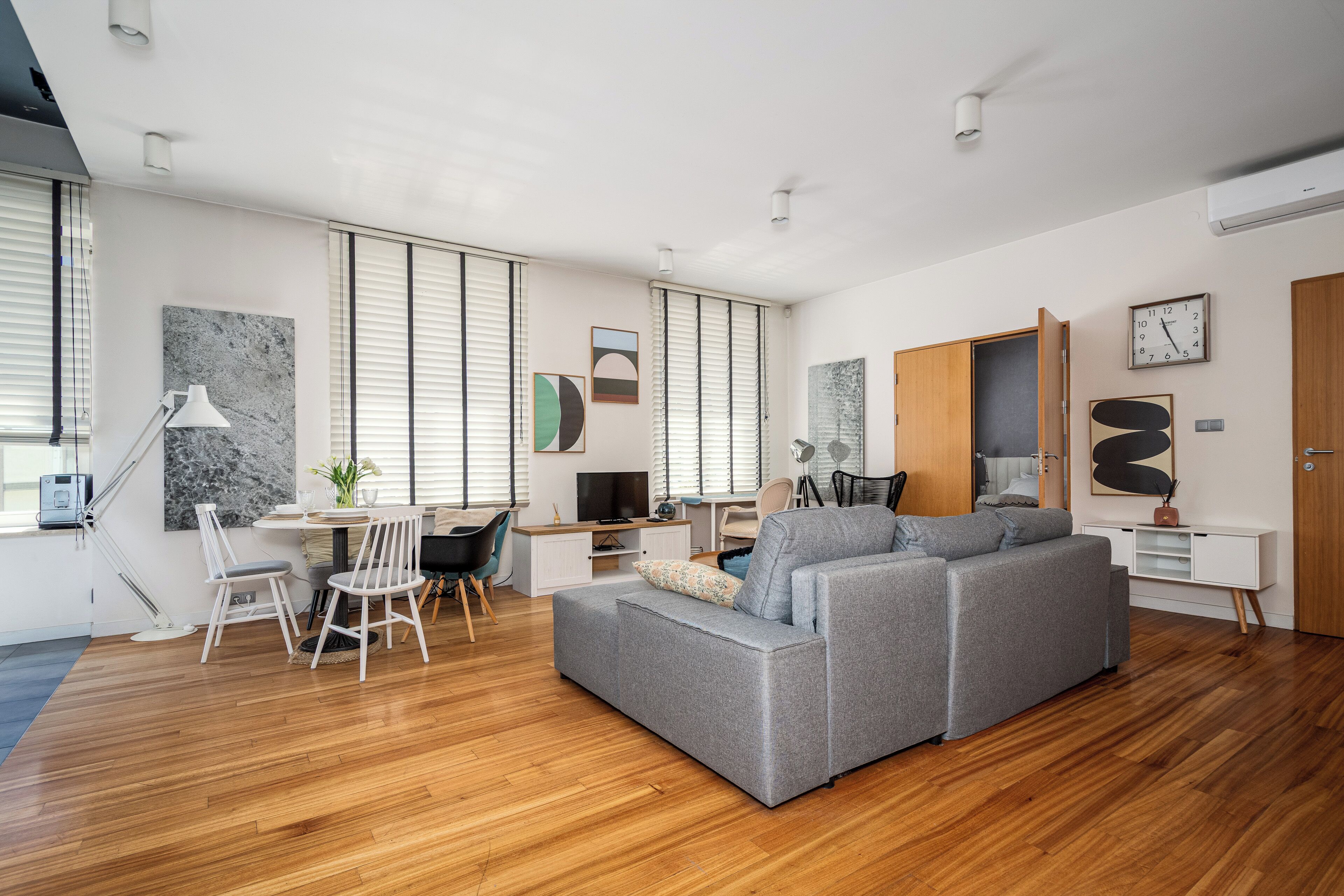 A modern living room with a grey sofa, wooden flooring, and a dining area with a table and chairs.