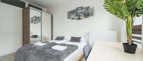 A bedroom with a bed, bedside tables, a large potted plant, and artwork on the wall.
