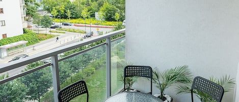 Un balcón con una mesa redonda de vidrio y cuatro sillas, con vistas a un paisaje urbano con edificios y vegetación.