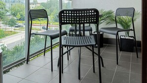 En balkong med två stolar och ett litet bord, med utsikt över en väg och några byggnader.