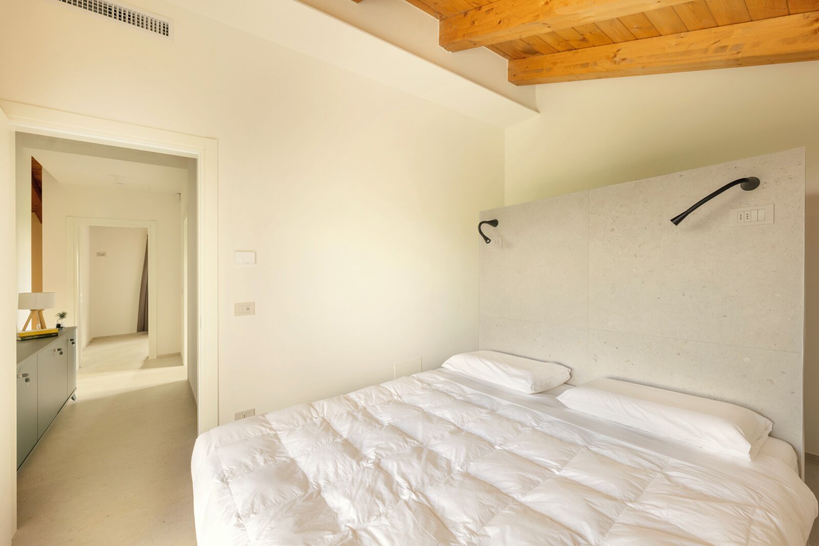 A bedroom with a bed, a wooden ceiling, and a door leading to another room.