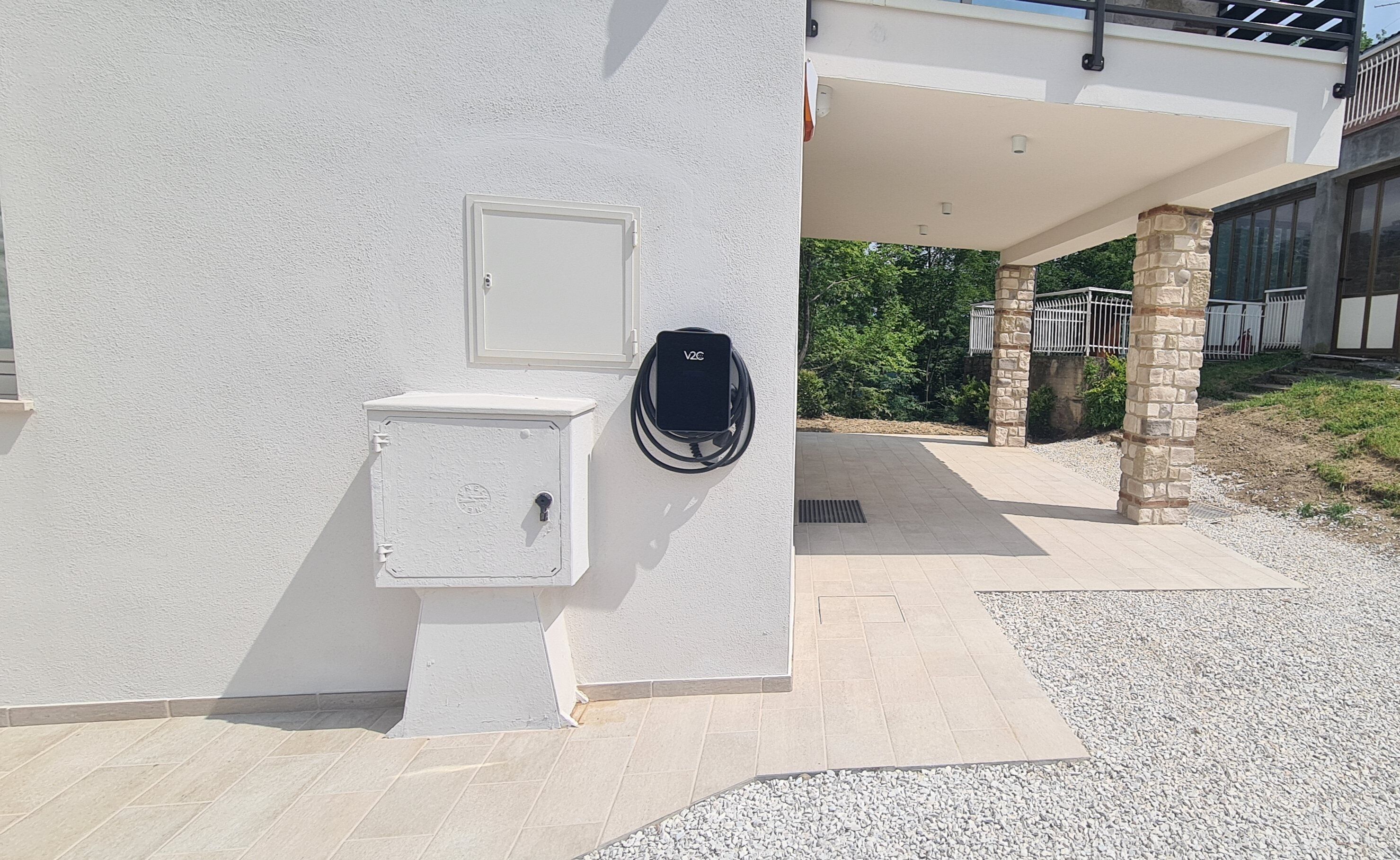 Une armoire de distribution électrique et une borne de recharge V2G fixées sur un mur blanc.