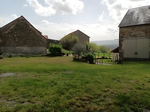 Une cour bordée de bâtiments en pierre, une pelouse et un garage en métal.