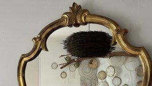 Ett sovrum med en säng, kuddar, ett sängbord, en spegel med en utsmyckad ram och väggdekorationer, inklusive drömfångare och en lykta.