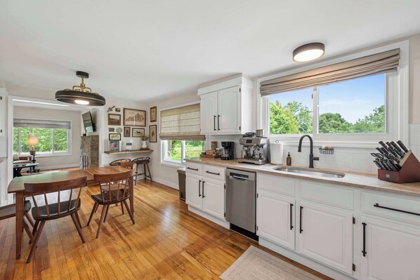 A modern kitchen with white cabinets, a wooden dining table, and a large window. - 3BR Stone Farm House, Parking, Grill, Laundry (Florence)