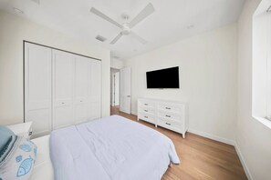Ein Schlafzimmer mit einem Bett, einem Kleiderschrank, einer Kommode, einem Deckenventilator und einem an der Wand montierten Fernseher.