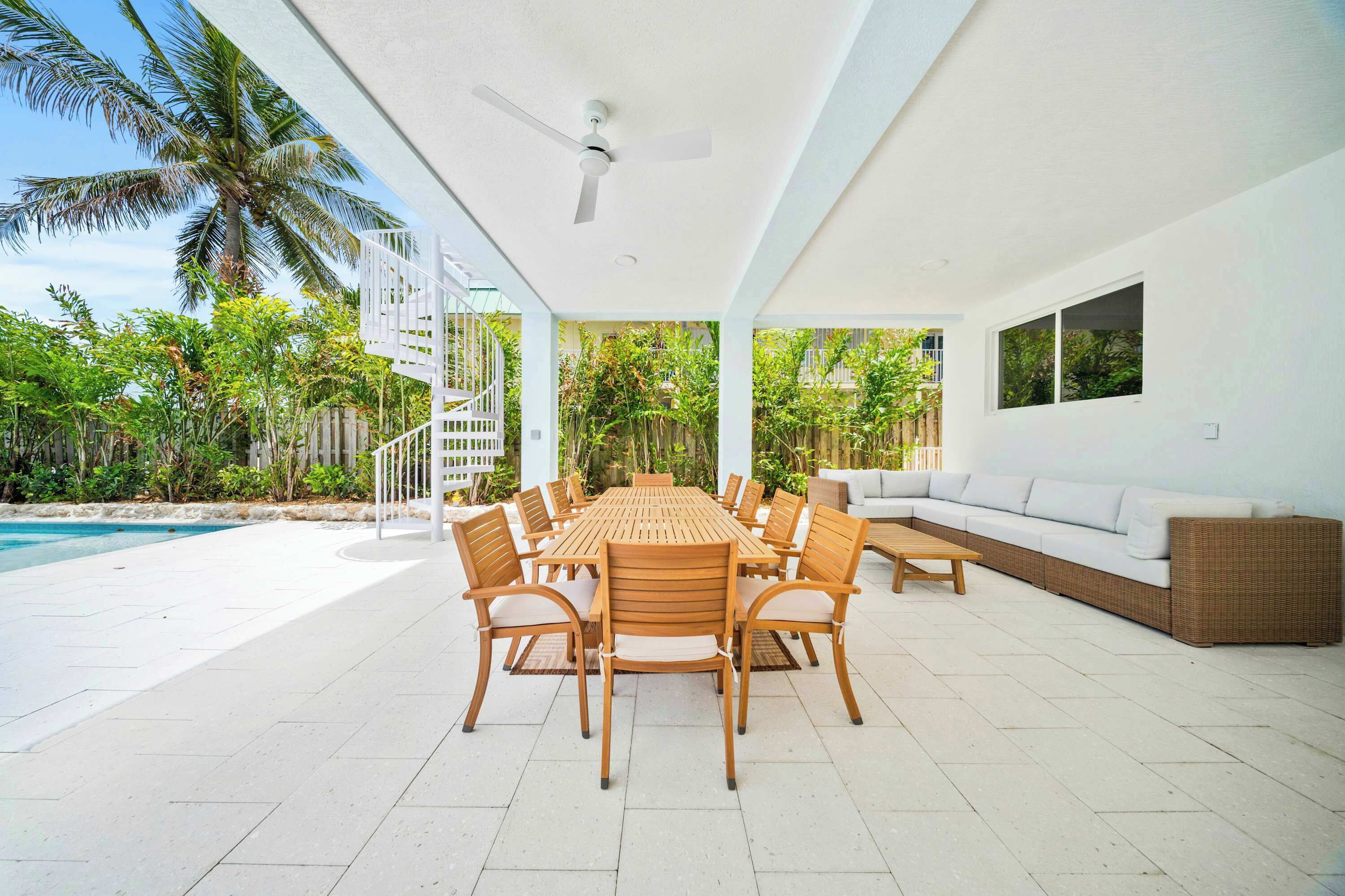 A covered outdoor dining area with a pool, wooden furniture, and lush greenery.