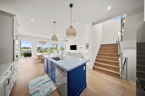 Une cuisine moderne dotée d’un îlot central, de luminaires suspendus et offrant une vue sur l’extérieur.