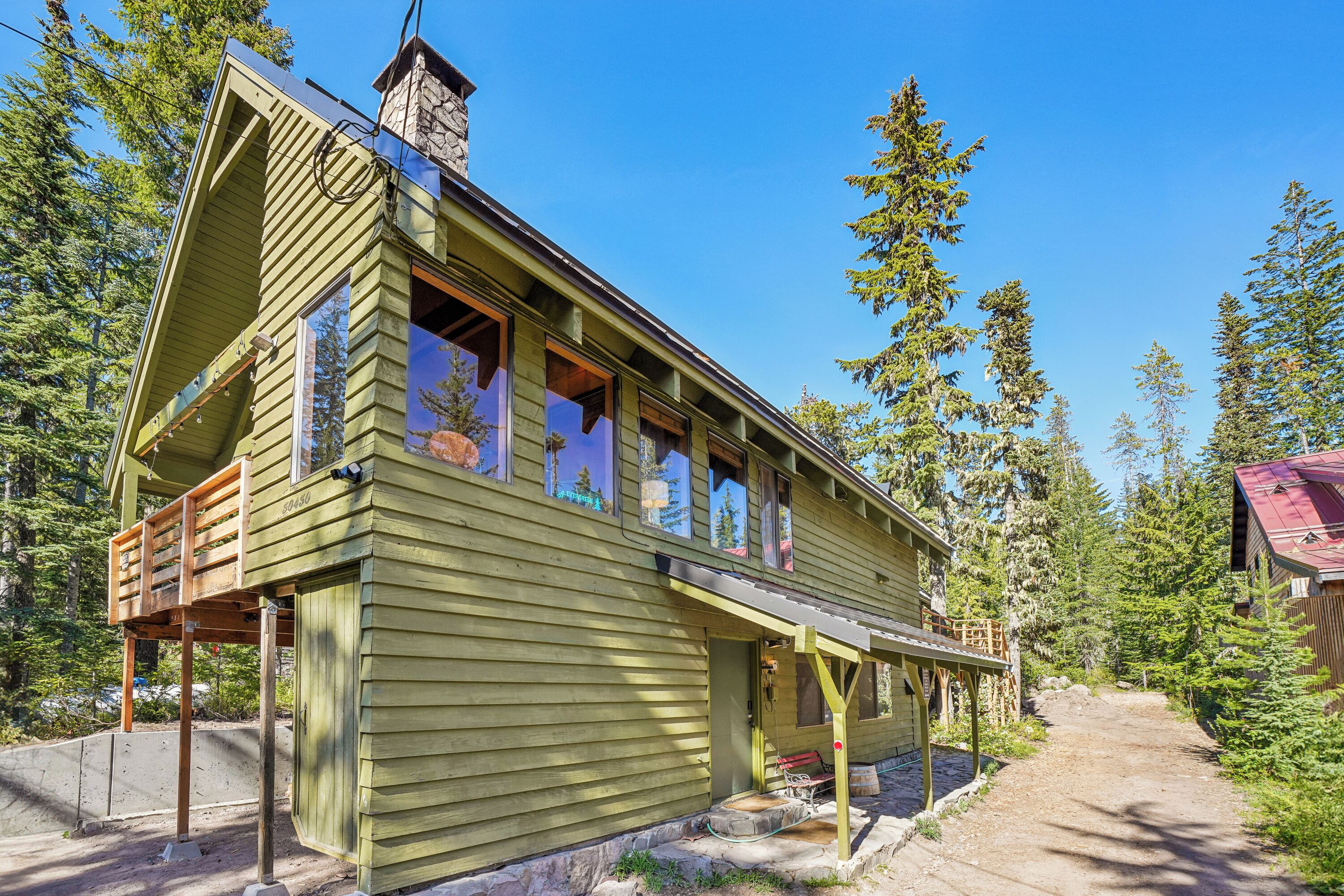 A green wooden cabin with a porch, large windows, and a chimney.
