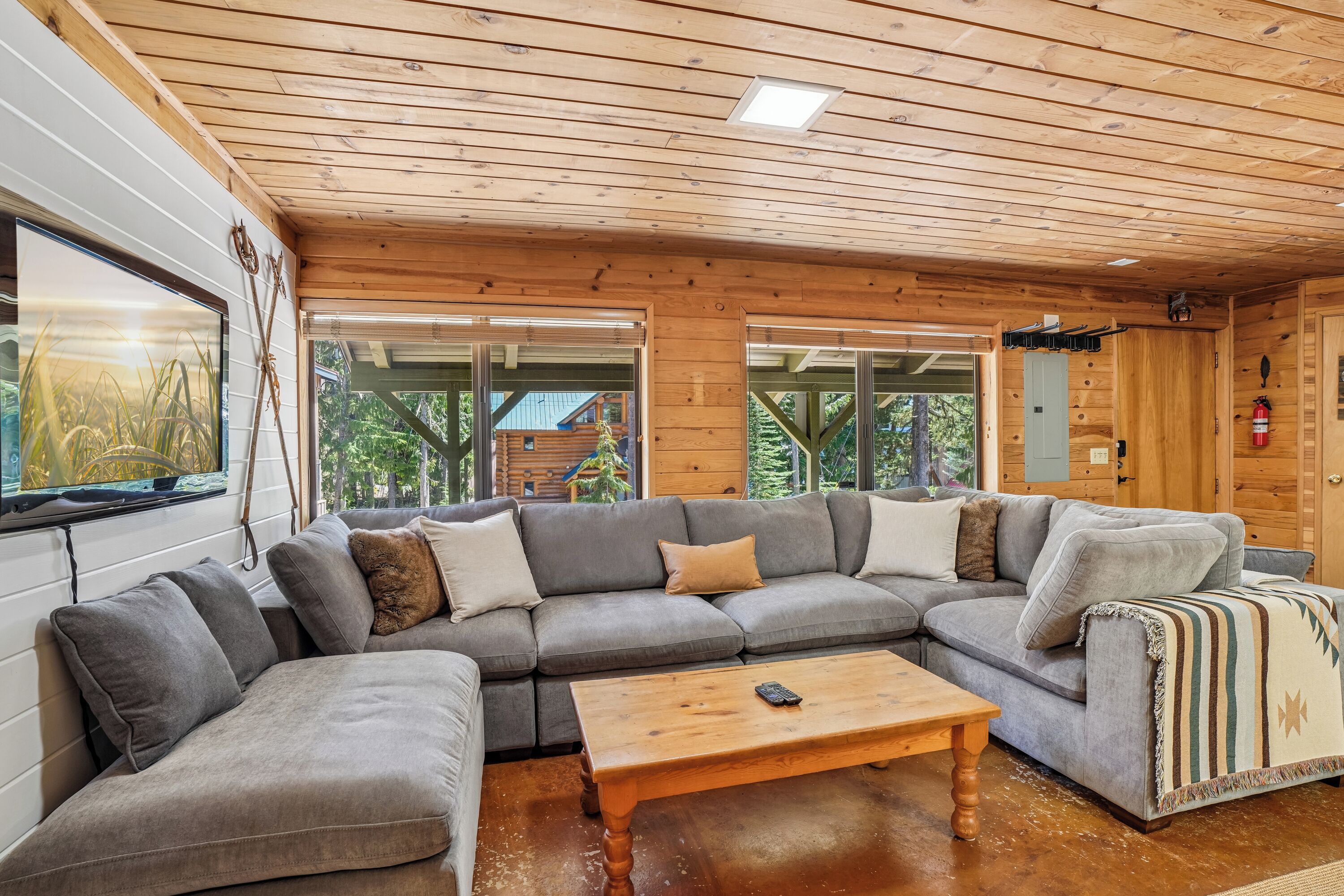 L’intérieur d’un chalet moderne en bois, doté d’un canapé d’angle, d’une table basse en bois et de grandes fenêtres offrant une vue sur la forêt environnante.