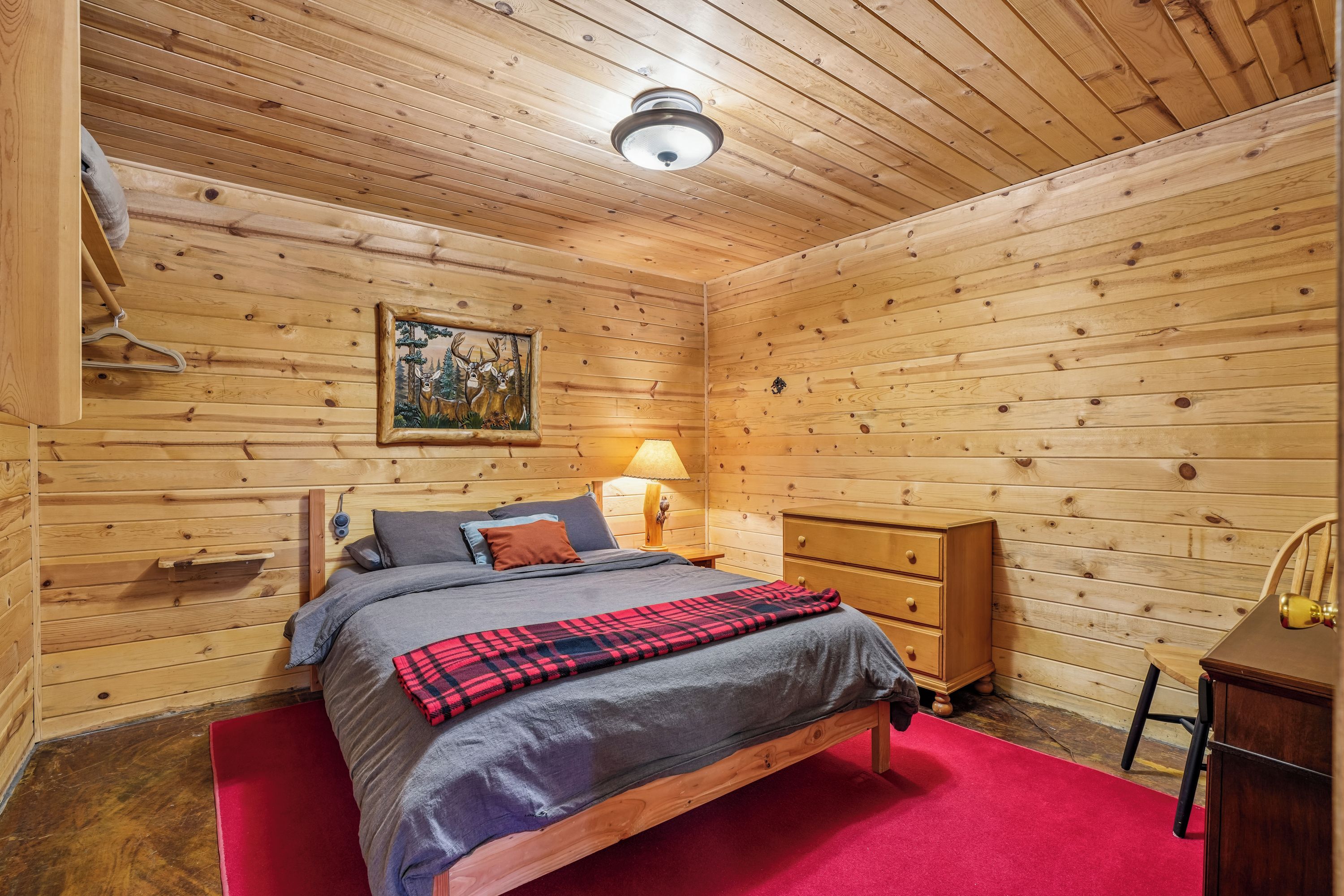 Une pièce aux murs lambrissés, comprenant un lit, une table de chevet, une lampe et une commode.