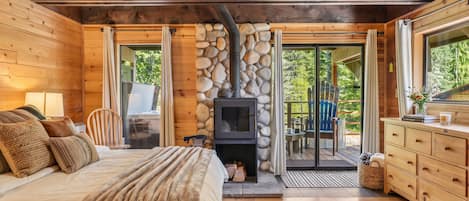 A cozy cabin interior with a bed, a fireplace, a dining area, and a view of the outdoors.