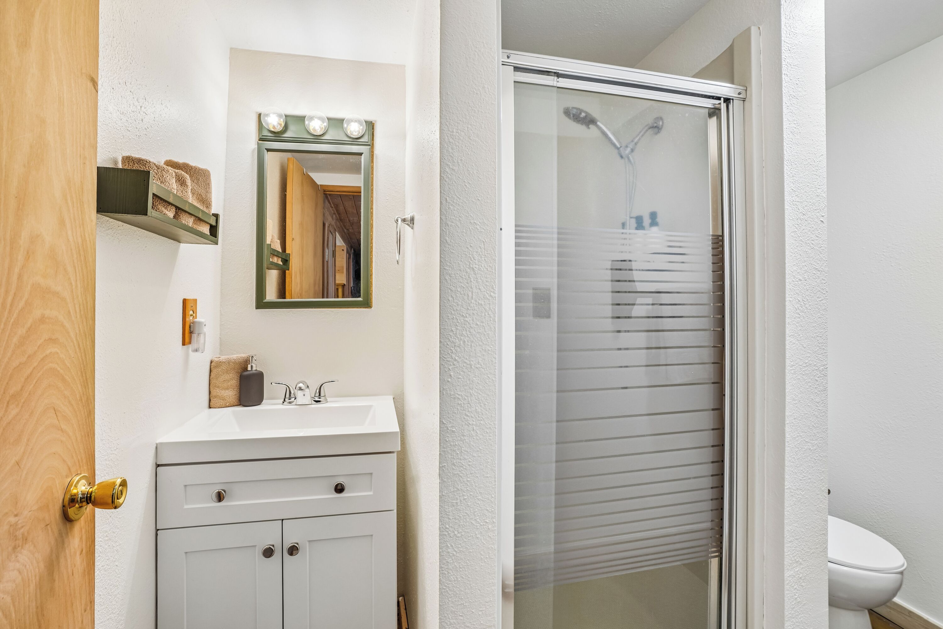 A bathroom with a white sink, a mirror with lights, a shower with a glass door, and a toilet.