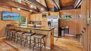A spacious kitchen with wooden cabinetry, a stainless steel refrigerator, and a bar area with stools. - Govy 4BR•Ski-In/Out•Hot Tub•2 Living Rooms (Government Camp)
