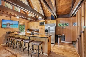 A spacious kitchen with wooden cabinetry, a stainless steel refrigerator, and a bar area with stools.