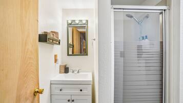 Une salle de bain avec un lavabo blanc, un miroir avec éclairage intégré, un porte-serviettes et une douche dotée d’une porte en verre.