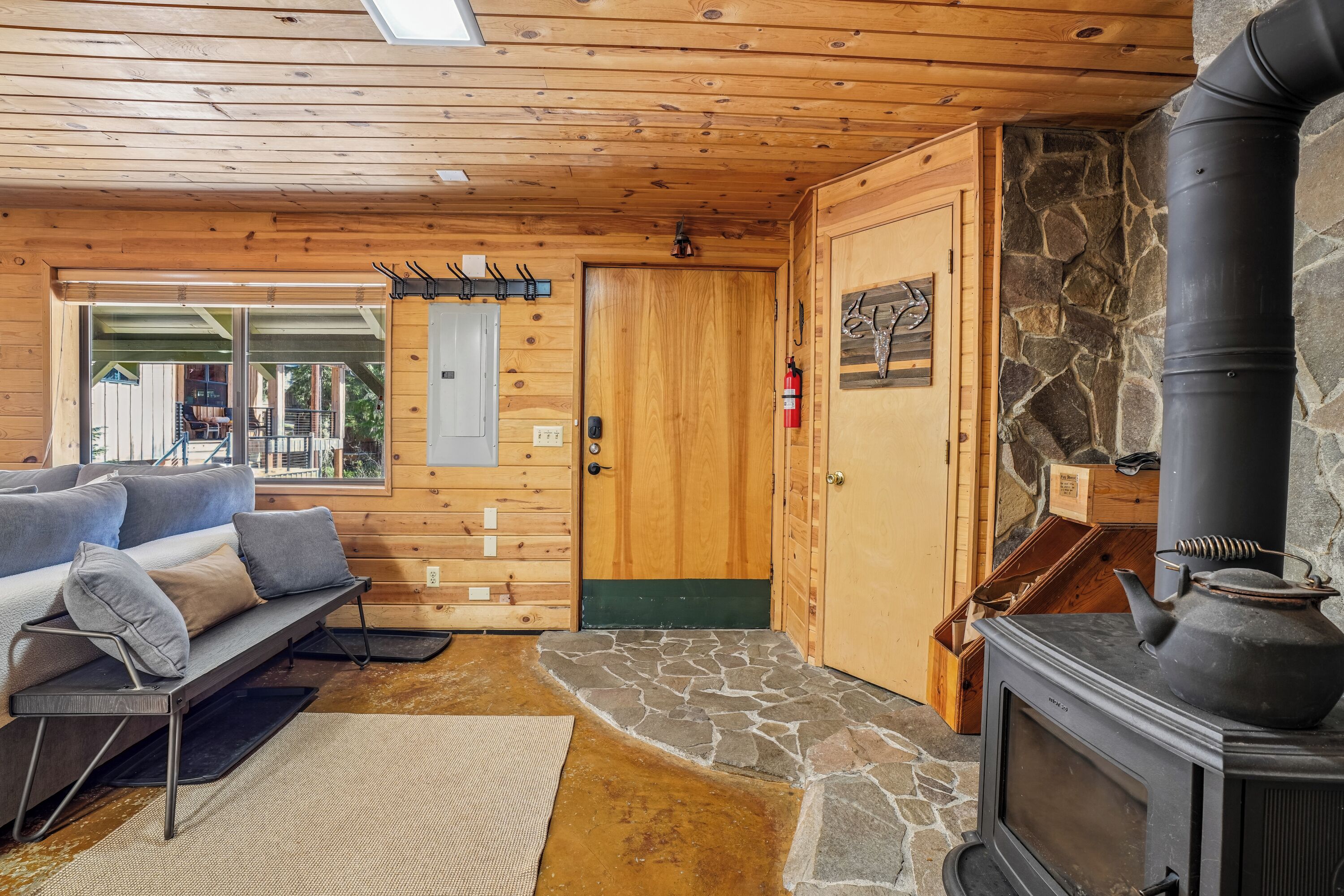 L’intérieur d’un chalet accueillant, avec une cheminée en pierre, une porte en bois et un canapé agrémenté de coussins.