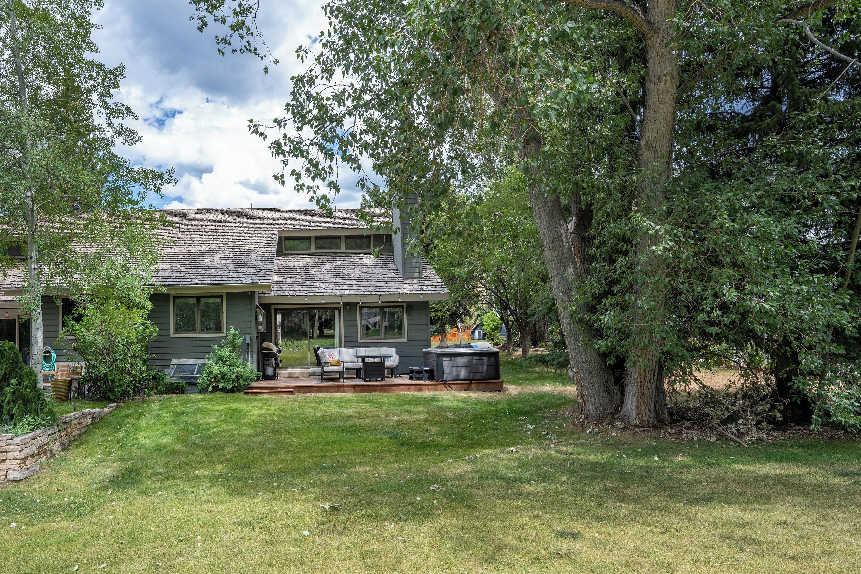 A residential property with a covered patio, outdoor furniture, and a large tree.