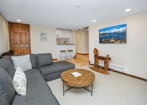 Ein Wohnzimmer mit grauem Sofa, einem Holztisch und einem Gemälde, das eine Küstenlandschaft zeigt.