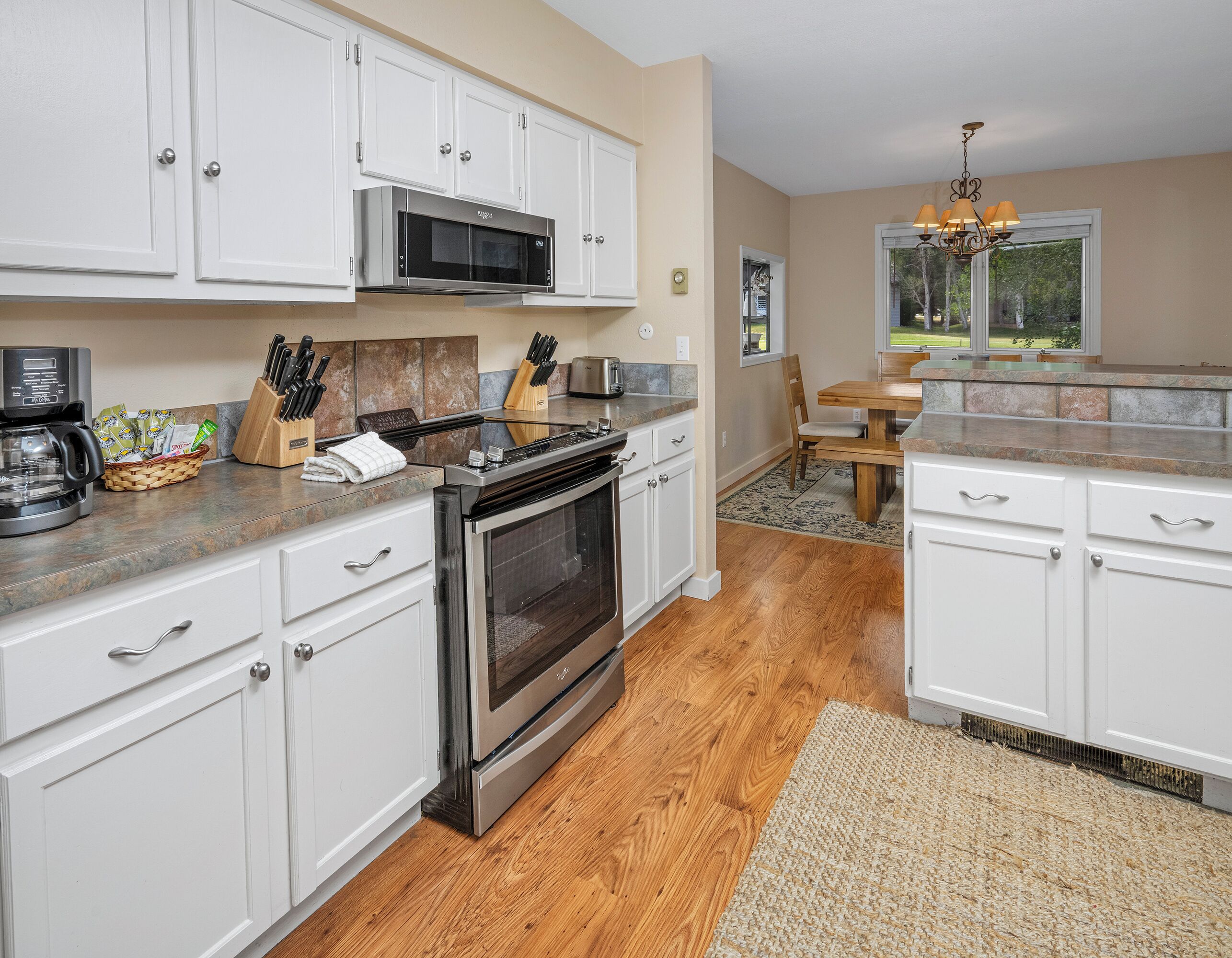 A modern kitchen with white cabinets, stainless steel appliances, and a wooden floor.
