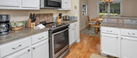A modern kitchen with white cabinets, stainless steel appliances, and a wooden floor.