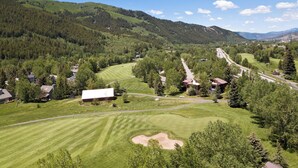 Um campo de golfe com um clube, rodeado por colinas arborizadas e um céu claro.
