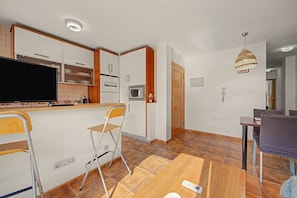 A compact kitchen with a built-in microwave, a wooden dining table, and a bar area with stools.