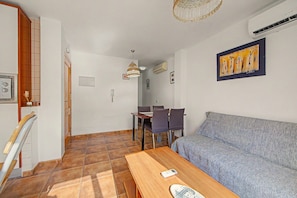 A living room with a sofa, a dining table with chairs, a wooden coffee table, and a hanging light fixture.