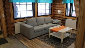 A log cabin interior with a grey sofa, a white table, and a patterned rug.