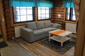 A log cabin interior with a grey sofa, a white table, and a patterned rug.