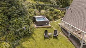 A hot tub in a lush garden with a deck and two Adirondack chairs.