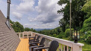 Eine Terrasse mit Holzgeländern und schwarzen Stühlen, mit Blick auf eine üppige grüne Landschaft und ferne Berge.