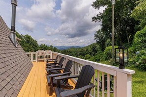 A deck with wooden railings and black chairs, overlooking a lush green landscape with mountains in the distance. - Fontana Hideout - Mtn Views | Hot Tub | Tail of the Dragon | Fontana Village Amenities (Fontana Dam)
