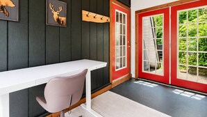 Ein Zimmer mit einem weißen Schreibtisch, einem grauen Stuhl, einer roten Tür und einer schwarzen Wand mit einem Bild von einem Hirsch.