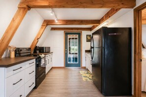 A kitchen with a black refrigerator, wooden beams, white cabinets, and a window with a view. - Fontana Hideout - Mtn Views | Hot Tub | Tail of the Dragon | Fontana Village Amenities (Fontana Dam)