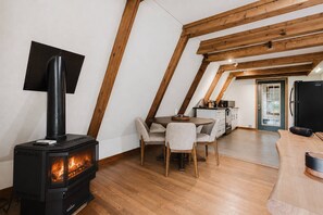 A cozy loft bedroom with a wood-burning stove, a dining area with a table and chairs, and a kitchenette.