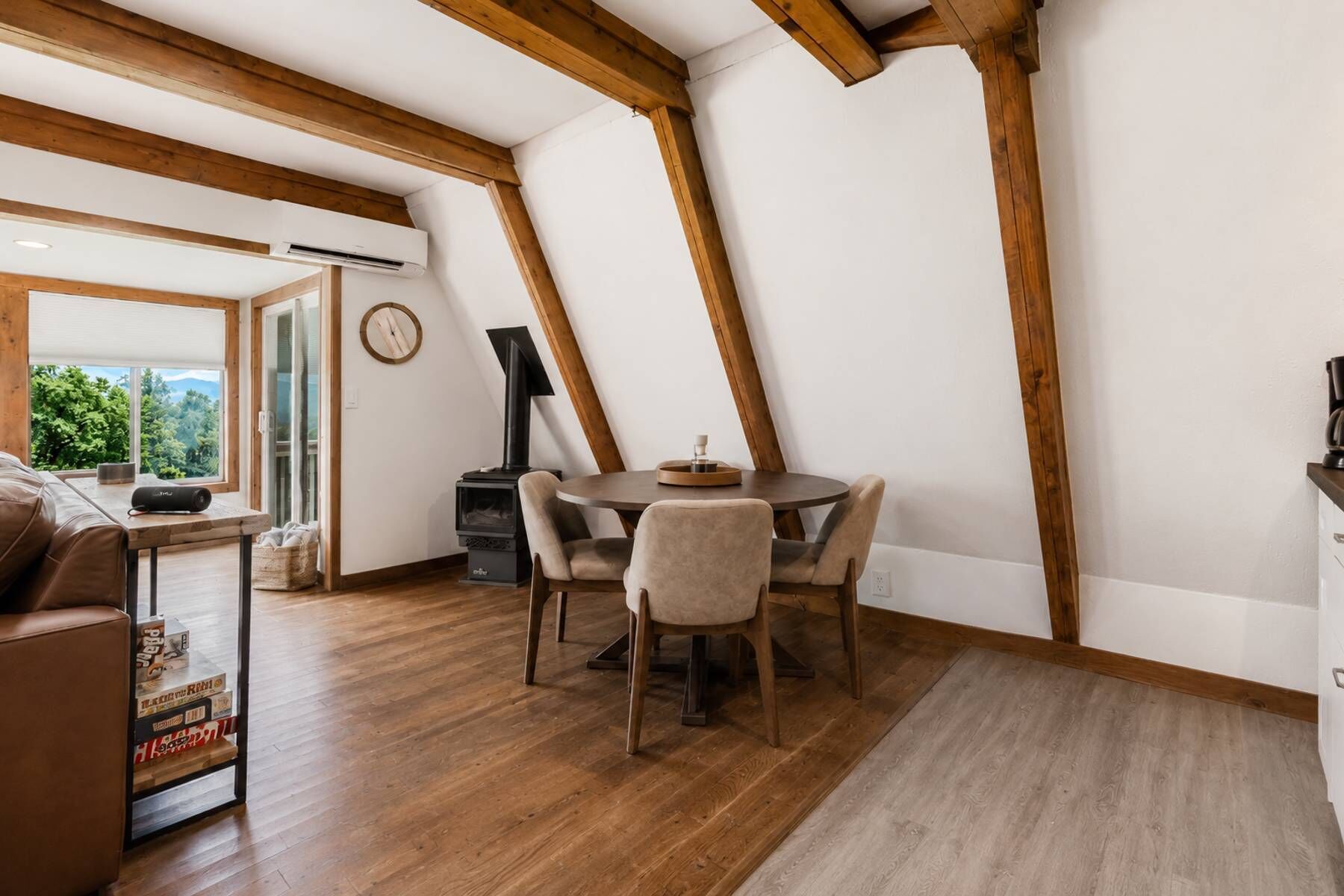 Een knus vertrek met houten plafond, een ronde tafel met stoelen, een open haard en een raam met uitzicht op groen.