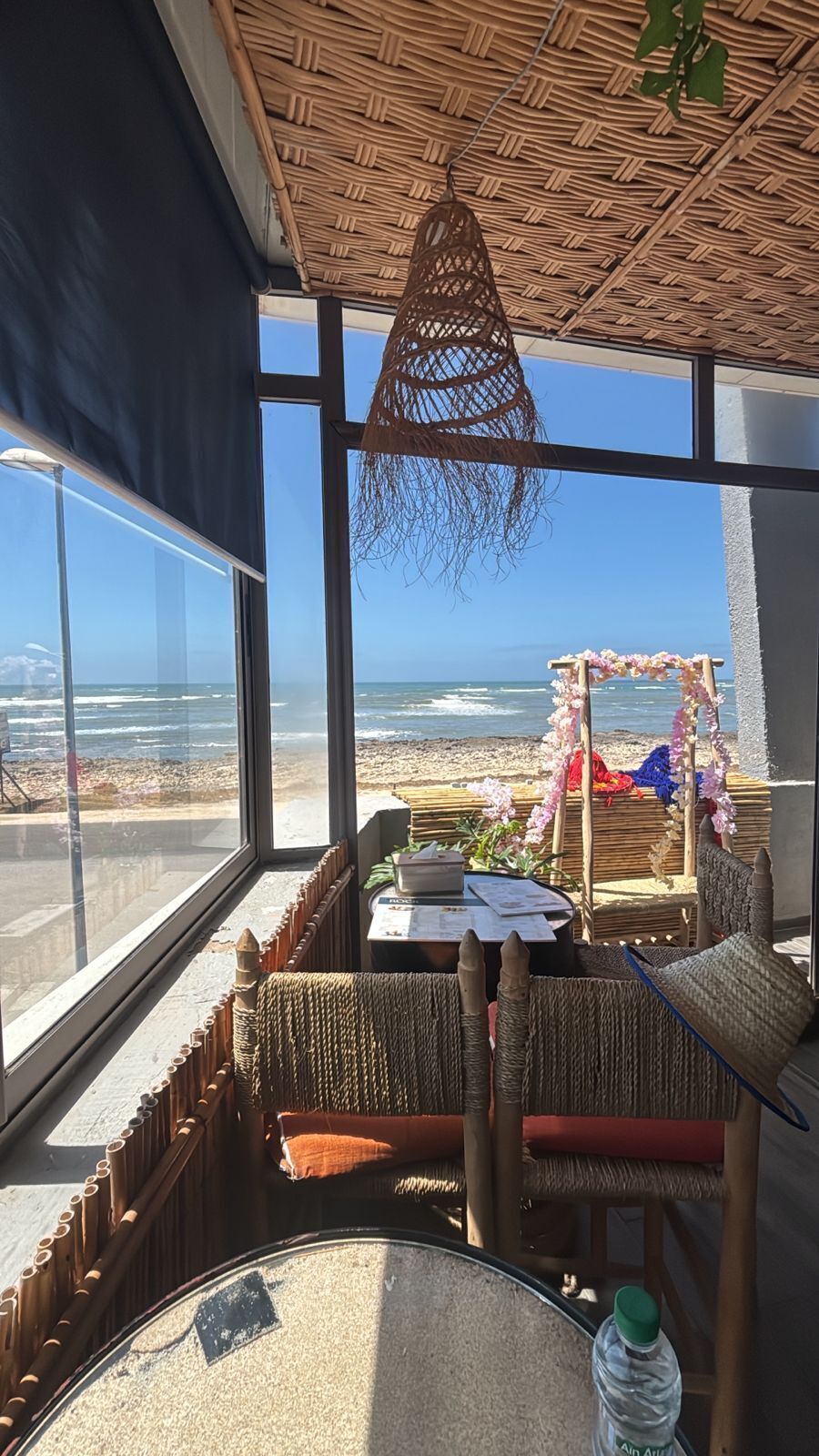 A room with a view of the beach, a table with a menu, and a hanging light fixture.